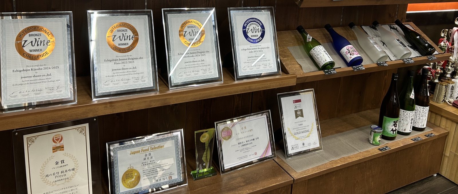 事務所の棚に並ぶIWCや美酒コンクールの賞状と商品