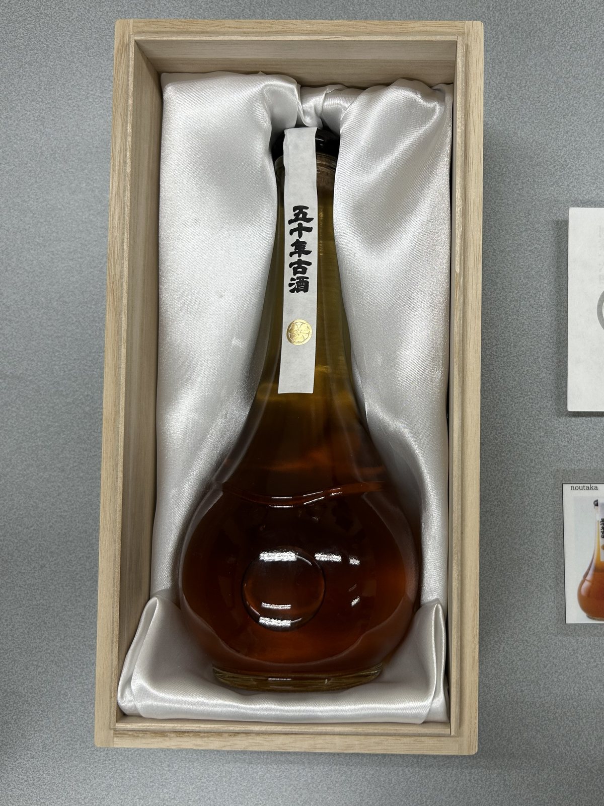 桐箱に入った五十年古酒。琥珀色の酒が500mlの瓶に入っている
